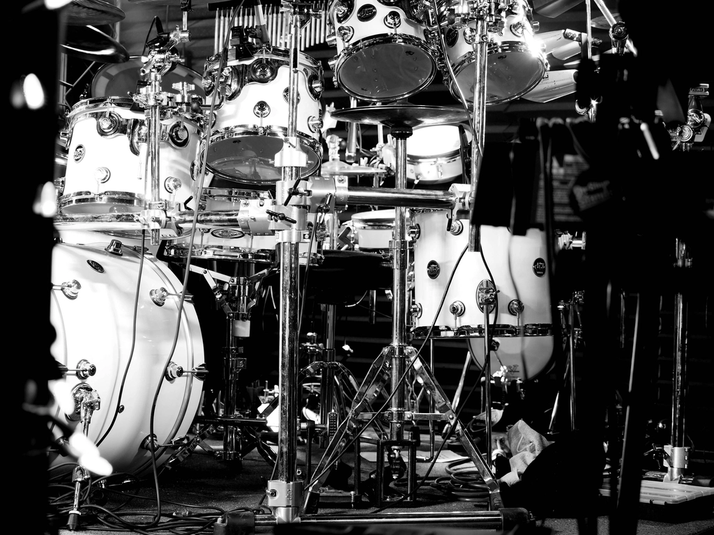 Black-and-white photograph of a large multi-piece drum kit on stage.